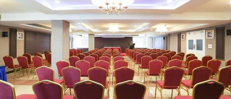 A conference room with rows of red chairs and a podium at the front.