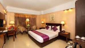Habitación de hotel con una cama grande, dos mesitas de noche, un escritorio con una silla, televisión y un rincón para café.
