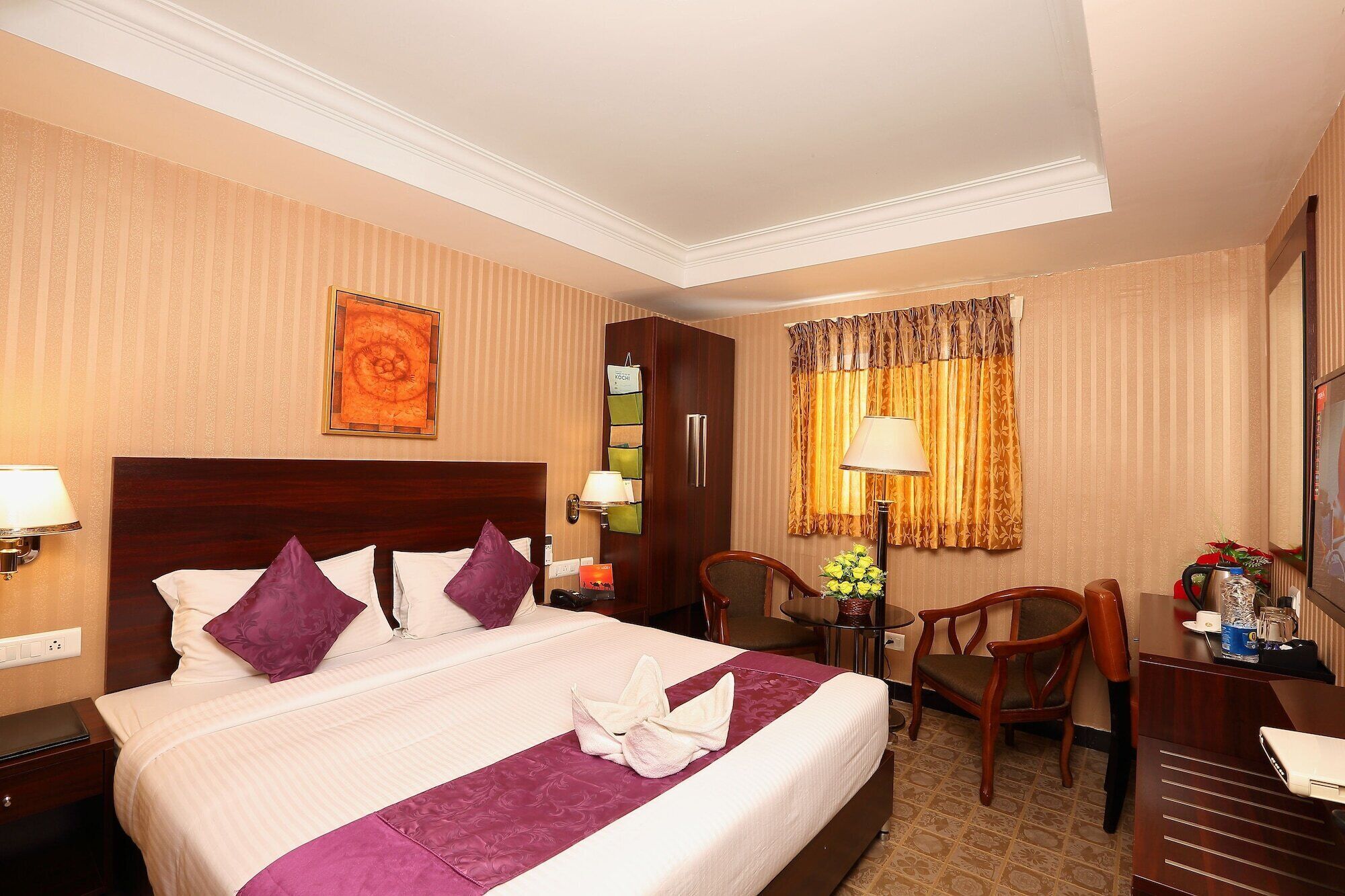A hotel room with a large bed, a desk, a chair, and a small table with a lamp.