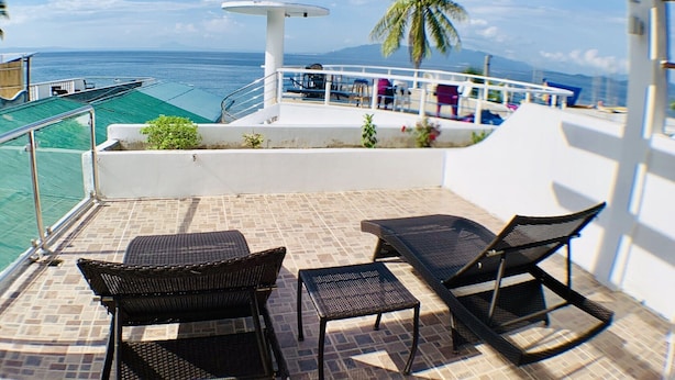 A balcony with wicker furniture, a palm tree, and a view of the ocean. - Arkipelago Beach Resort (Puerto Galera)