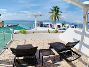 A balcony with wicker furniture, a palm tree, and a view of the ocean. - Arkipelago Beach Resort (Puerto Galera)