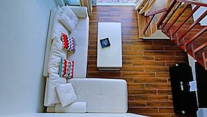A modern living room with a white sofa, colorful pillows, a white coffee table, and a wooden floor. - Arkipelago Beach Resort (Puerto Galera)