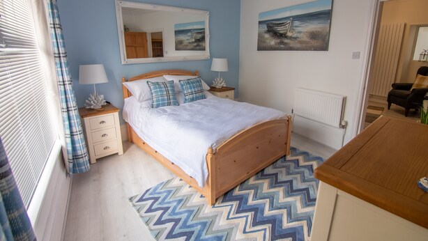A bedroom with a wooden bed, a nightstand, a dresser, a mirror, and a painting on the wall.