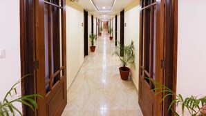 A hotel hallway with wooden doors, potted plants, and a marble floor. - Treebo Nand Residency (Dehradun)