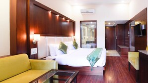 A hotel room with a bed, a sofa, a TV, and a bathroom visible through an open door. - Treebo Nand Residency (Dehradun)