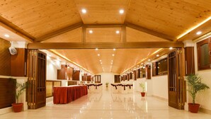 A spacious, well-lit hall with a high wooden ceiling and a long table set for a formal event. - Treebo Nand Residency (Dehradun)