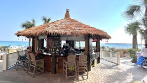 Eine Strandbar mit einem Reetdach, Holzsesseln und einer Speisekarte, die Getränke auflistet.