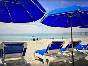 Uma praia com guarda-sóis azuis e cadeiras de praia brancas.