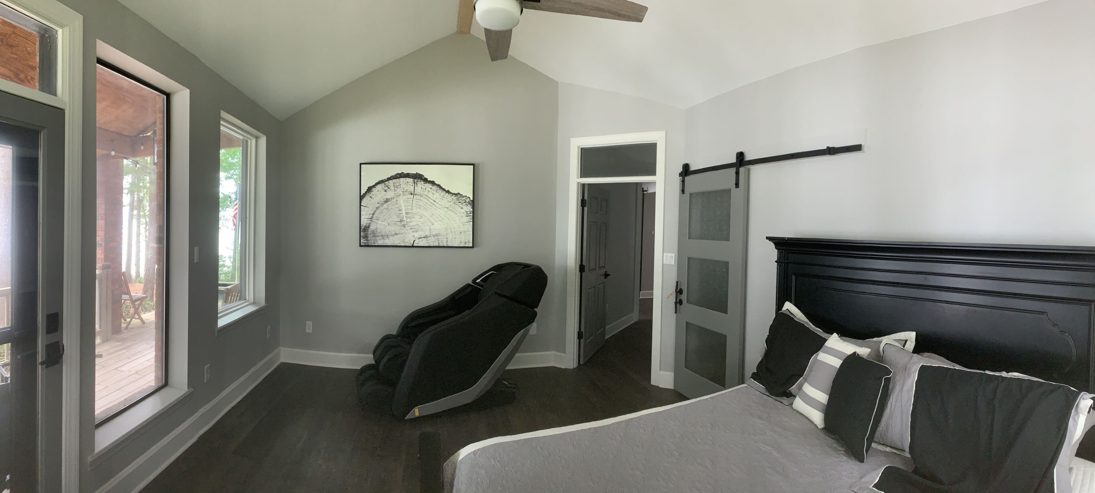 A bedroom with a bed, a massage chair, a large window, and a door leading to another room.