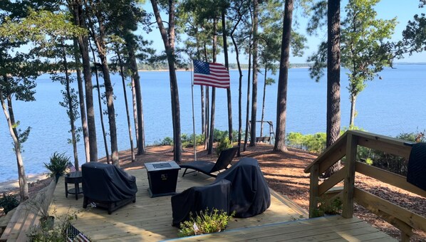 A deck with outdoor seating, a flag, and a view of the water. - Eagles Point! Incredible Private Waterfront 3.5 acres. Long range water views! (Zavalla)