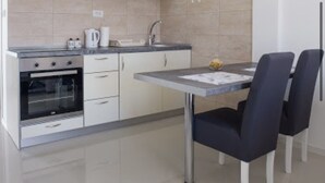 A modern kitchen with white cabinets, a built-in oven, a sink, and a dining table with chairs. - ♥Apartmani Kankaras | Sea View - Quiet Quarter♥ (Tivat)