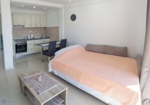 A modern bedroom with a large bed, a small desk, and a kitchenette in the background. - ♥Apartmani Kankaras | Sea View - Quiet Quarter♥ (Tivat)