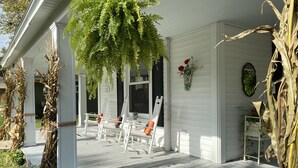 Eine Veranda mit weißen Holzgeländern, einem hängenden Farn und einem Blumenkasten mit roten Blüten.