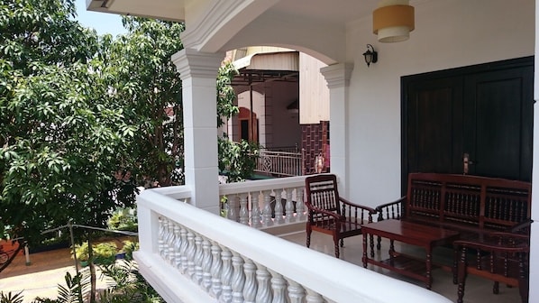 A balcony with white balustrades, wooden furniture, and a view of a building with a green door. - Dechasey Villa (Siem Reap)