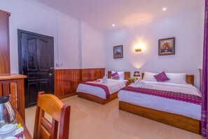 Habitación de hotel con dos camas, una silla de madera, una mesa con hervidor y una puerta.