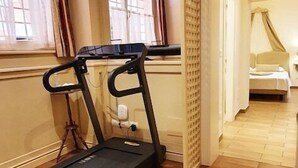 A room with a treadmill, wooden flooring, a window with curtains, and a bed with a canopy. - Casa Miramonte (Bologna)