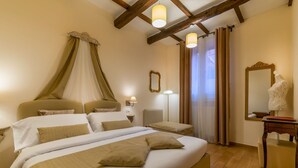A hotel room with a large bed, a canopy bed, a bedside table with a lamp, a mirror, and a wooden dresser. - Casa Miramonte (Bologna)