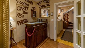 A cozy hotel lobby with a wooden reception desk, a staircase, and a wall decorated with various beverage and food items. - Casa Miramonte (Bologna)