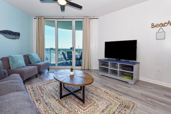 A living room with a sofa, a coffee table, a TV stand, and a balcony with a view. - Updated 5th Floor Condo w/ Fun Amenities at The Palms of Destin! 💚🥥🌴 (Destin)