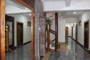 A hallway with marble flooring, wooden doors, and a staircase. - Hotel Presidency in Electronic City (Anekal)