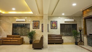 A lobby with marble walls, two sofas, potted plants, and framed artwork. - Hotel Presidency in Electronic City (Anekal)