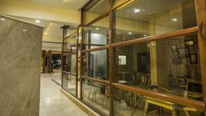 A modern interior with a marble column, wooden-framed glass windows, and a seating area with tables and chairs. - Hotel Presidency in Electronic City (Anekal)