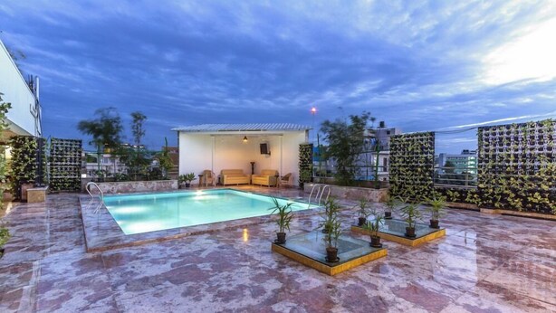 A rooftop pool area with a clear sky, a small seating area, and potted plants. - Hotel Presidency in Electronic City (Anekal)
