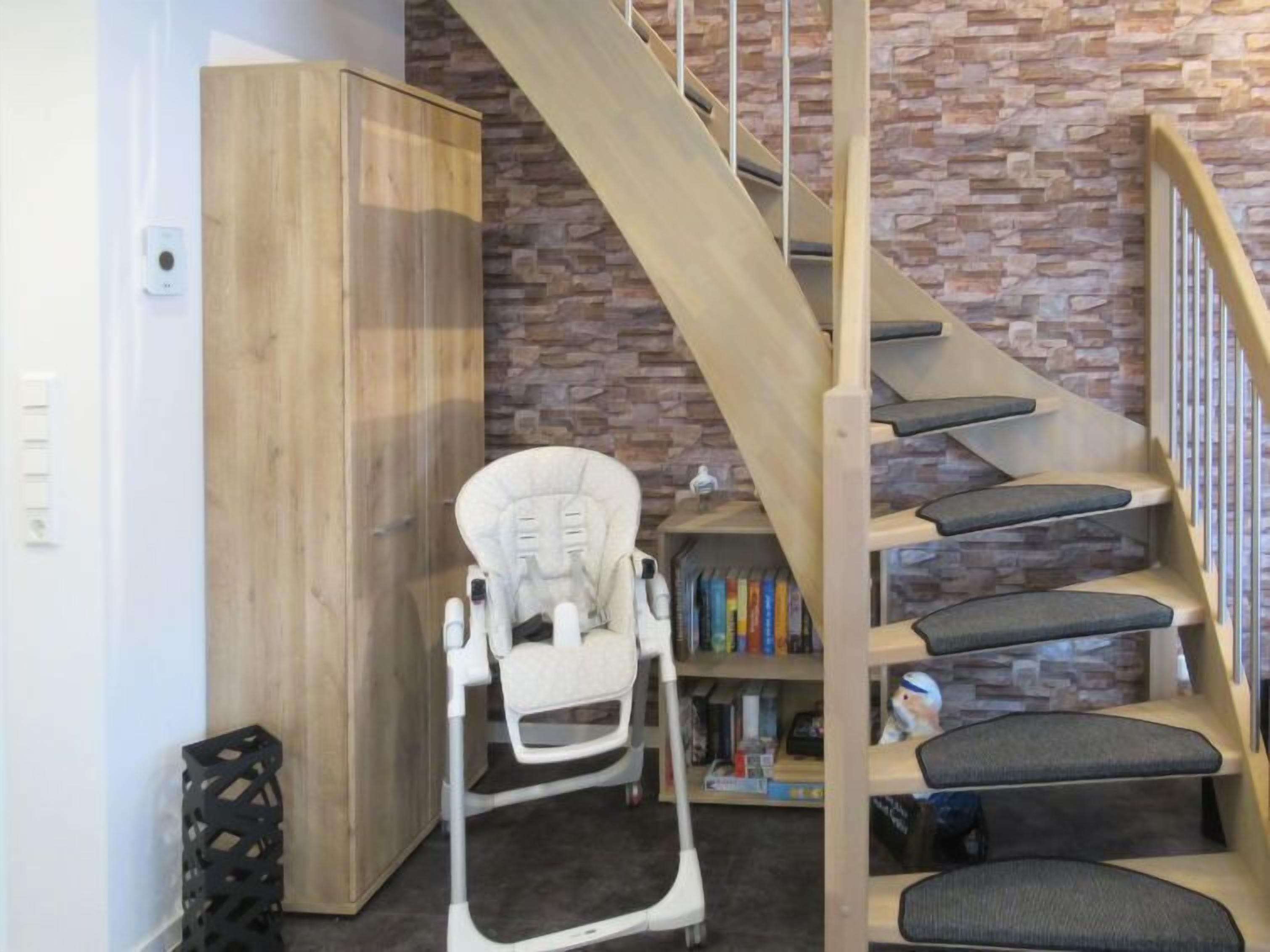 Ein modernes Interieur mit einer Holztreppe, einem weißen Babywippstuhl und einem Bücherregal mit Büchern.