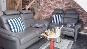 Ein modernes Wohnzimmer mit zwei grauen Ledersofas, einem Glastisch und einer Steinwand.