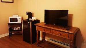 A compact living space with a wooden desk, a flat-screen TV, a microwave, and a coffee maker.