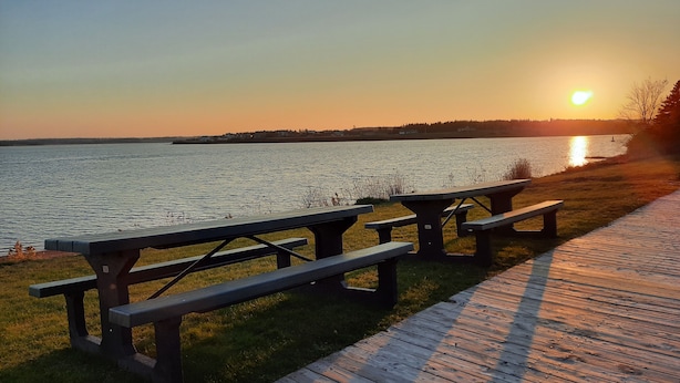 A wooden deck with picnic tables overlooking a body of water during sunset.