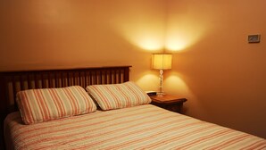 A neatly made bed with striped bedding, a wooden headboard, and a bedside table with a lamp and a clock.