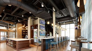 A modern bar area with a long counter, multiple seating options, and visible kitchen equipment in the background.