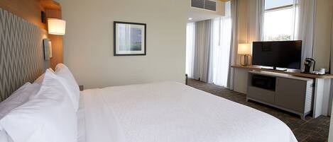 Habitación de hotel con una cama grande, televisión, escritorio con lámpara y un cuadro en la pared.