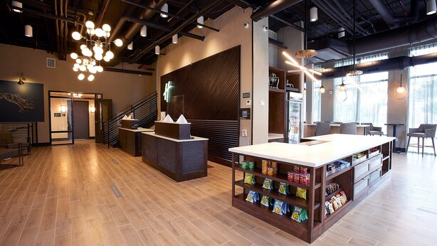 A modern hotel lobby with a reception desk, a seating area, and a snack bar.