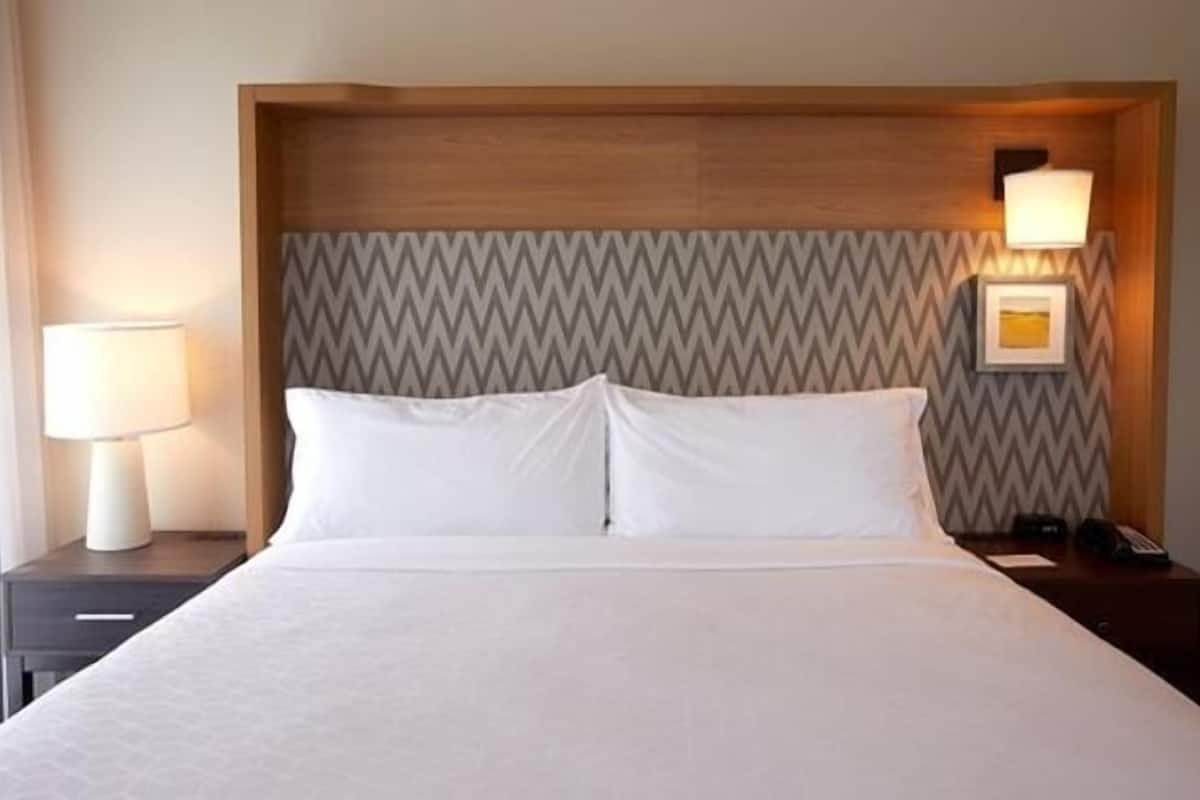A hotel room with a bed, nightstands, a lamp, and a wall-mounted light fixture.