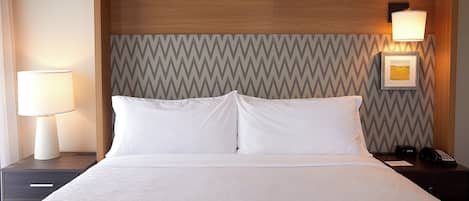 Una habitación de hotel con una cama, dos lámparas de noche, una mesita de noche, un reloj y un cuadro en la pared.