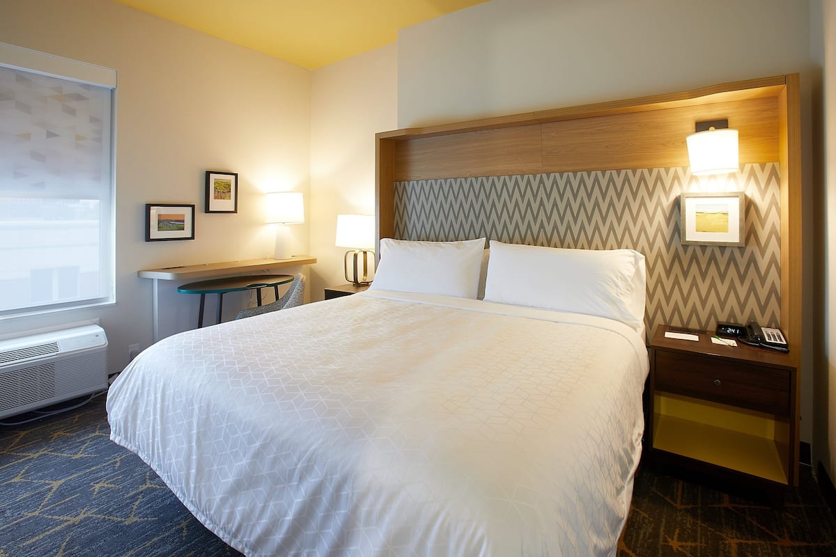 A hotel room with a large bed, a bedside table with a lamp, and a wall-mounted light.