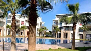 A modern hotel with a swimming pool, palm trees, and a well-maintained lawn. - Residence Hivernage Founty 5429 (Agadir)