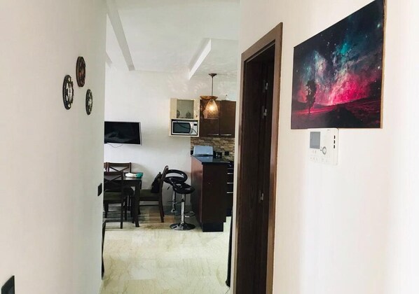 A narrow hallway leading to a kitchen with a dining area, a microwave, and a painting of a galaxy on the wall.