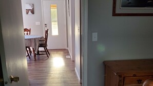 Un corridoio che conduce a una sala da pranzo con tavolo e sedie, pavimento in legno e una porta con finestra.