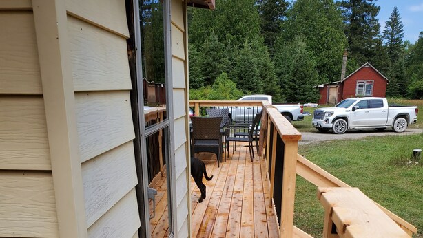 Un patio in legno con una porta vetrata che dà su una zona prendisole, circondato da una recinzione e un prato.