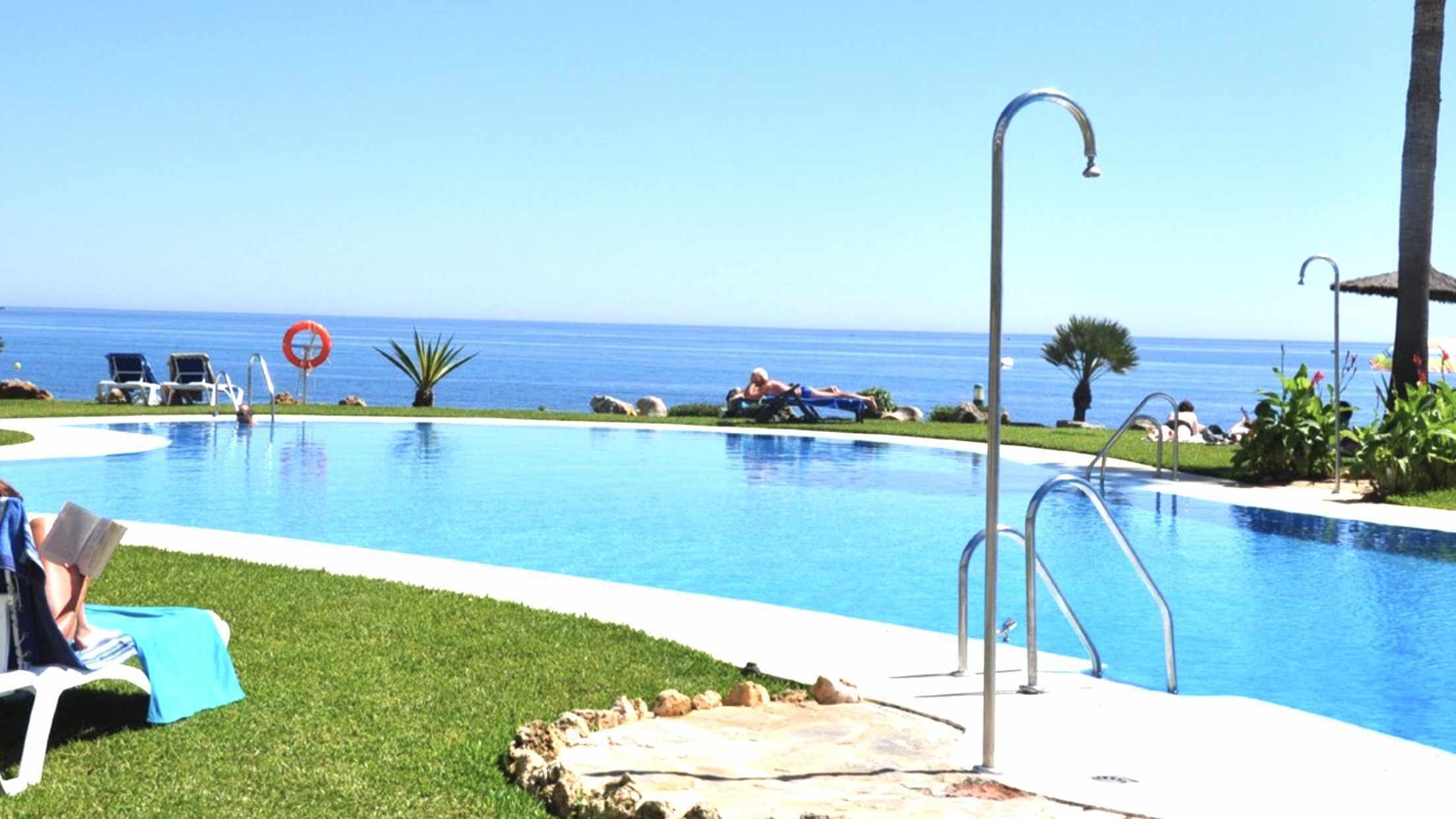 Una piscina con vista despejada al océano, sillas de descanso y un puesto de socorristas.