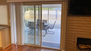 A living room with a sliding glass door leading to an outdoor patio area with a table and chairs. - Casa De La Roca (Albuquerque)