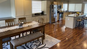 A modern kitchen with a central island, stainless steel appliances, and a dining area with a wooden table and bench. - Casa De La Roca (Albuquerque)