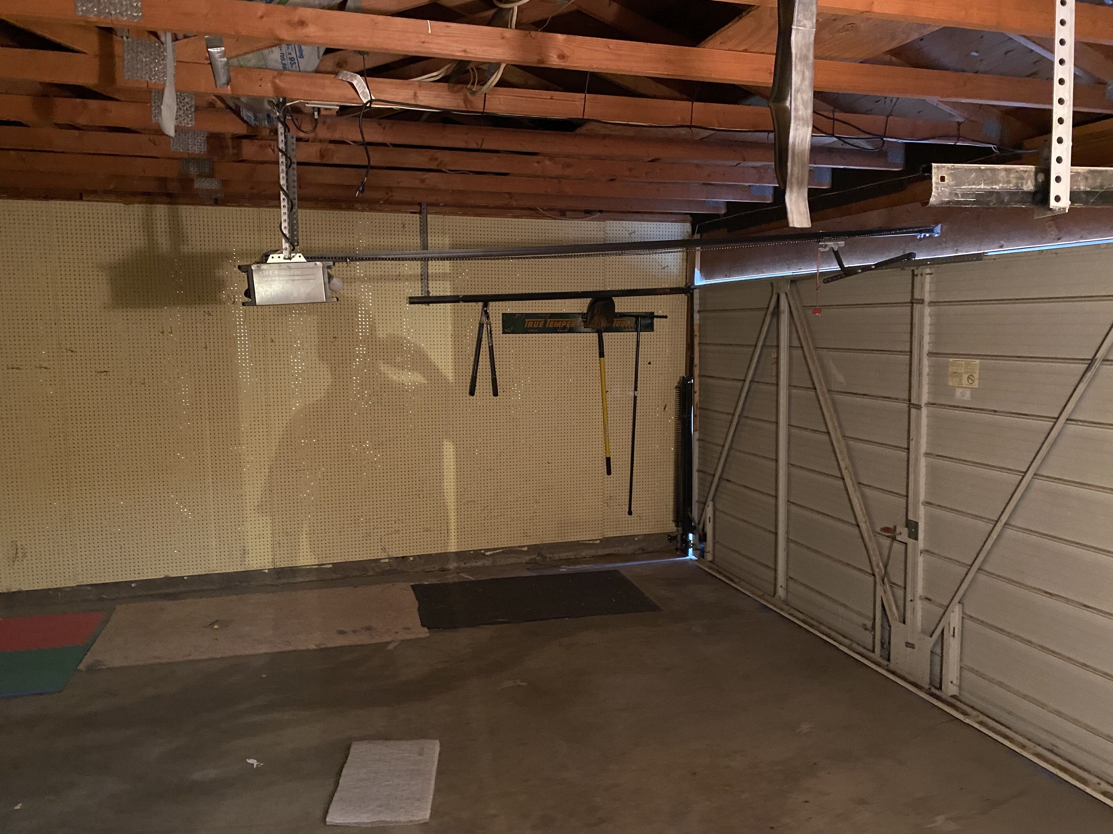 Un garaje con piso de hormigón, vigas de madera, pared con panel de tacos y puerta metálica.