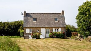 A stone house with a sloped roof, two windows, a door, and a small garage. There are two white chairs in the front yard. - Ker Kébec by Interhome (Crozon-Morgat)
