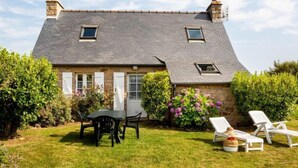 A stone house with a sloped roof, two small windows, a door, and a garden with a table and chairs. - Ker Kébec by Interhome (Crozon-Morgat)