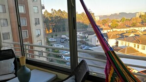 A balcony with a view of a residential area, a hammock, and a seating area with cushions and a vase.