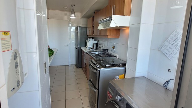 A modern kitchen with white tiles, stainless steel appliances, and wooden cabinets.